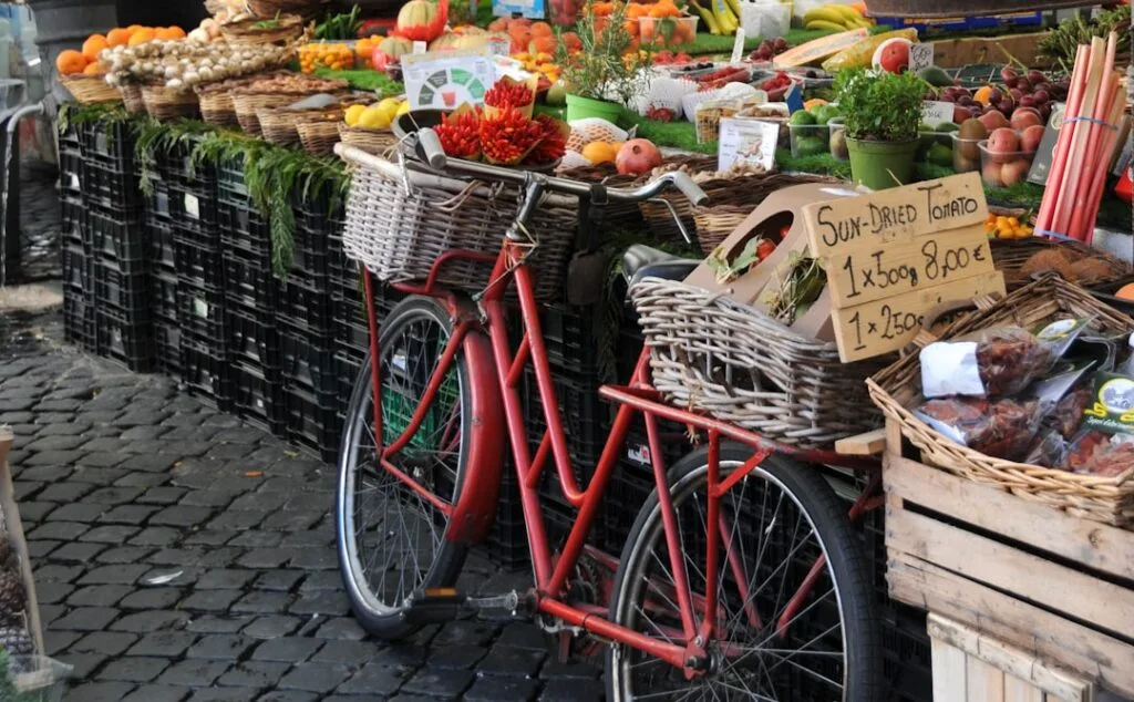 Vélo rouge à paniers appuyé contre un étal de fruits sur les pavés