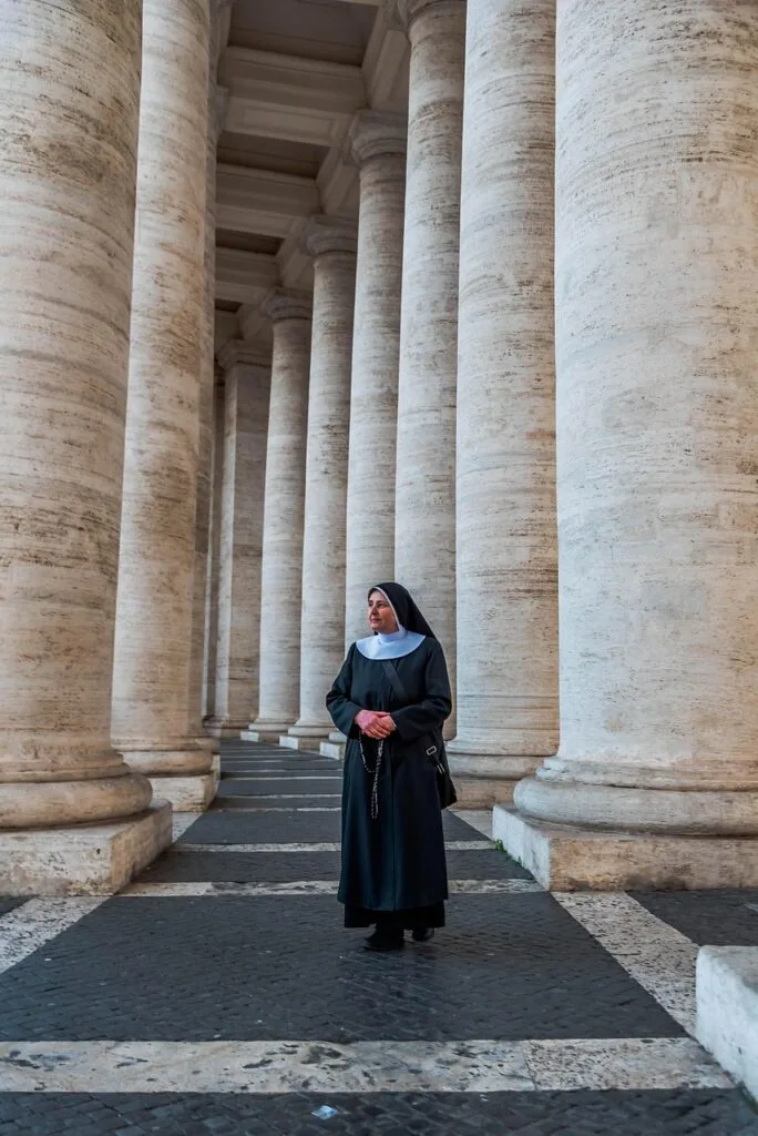 Une religieuse en habit tenant un chapelet parmi les colonnades de la place Saint-Pierre, Rome