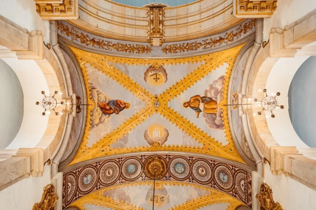 Painted vault with gilded patterns and chandeliers, church interior in Rome
