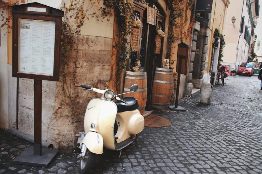 Vespa crème garée devant une trattoria sur une ruelle pavée de Rome