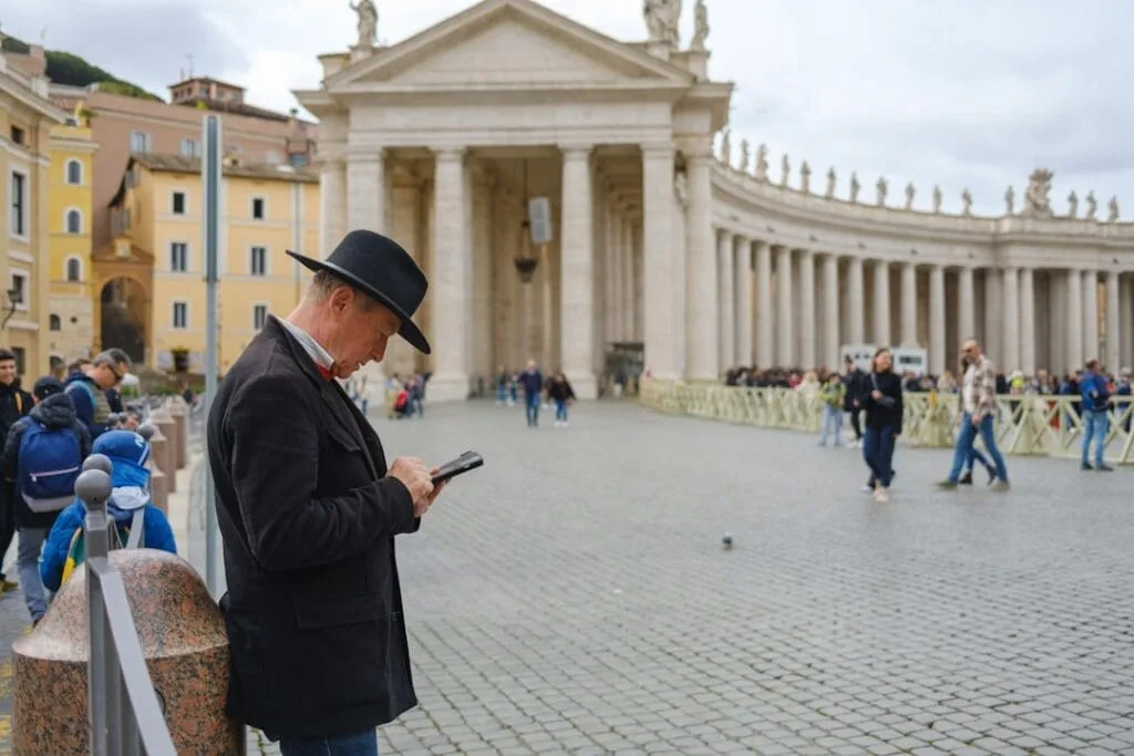 Homme chapeauté utilisant son téléphone sur la place Saint‑Pierre à Rome