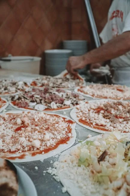 Pizzas en préparation recouvertes de sauce et fromage dans une pizzeria romaine