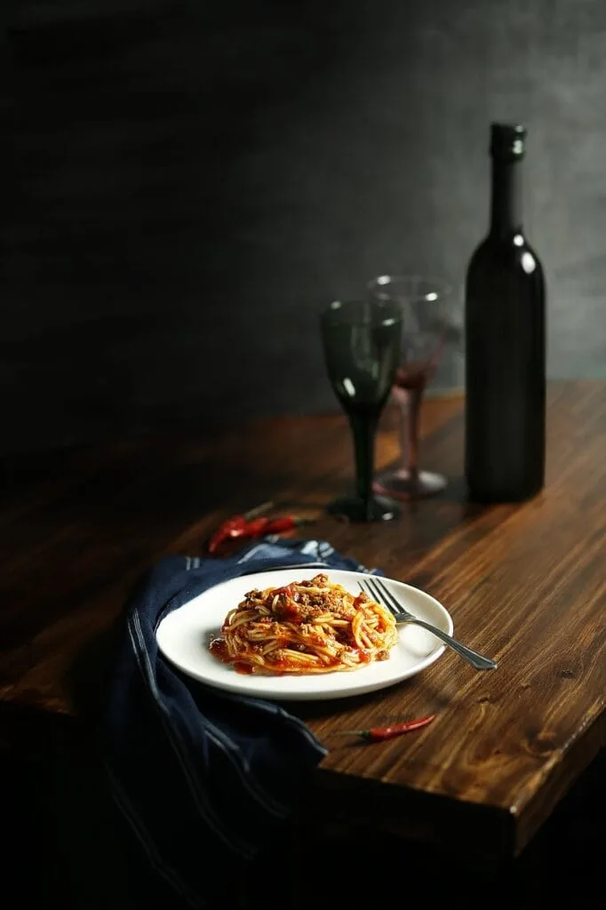 Assiette de spaghetti à la sauce tomate sur table en bois, bouteille de vin.