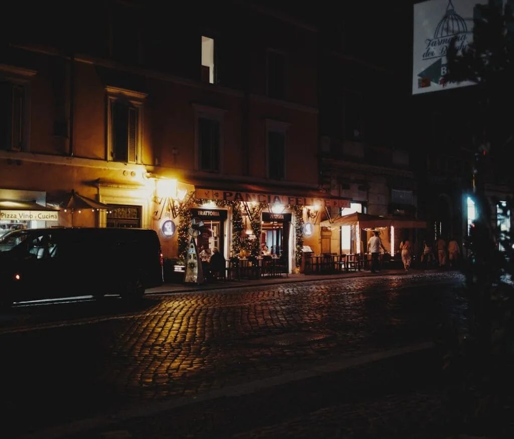 Façade de trattoria romaine éclairée la nuit, rue pavée humide