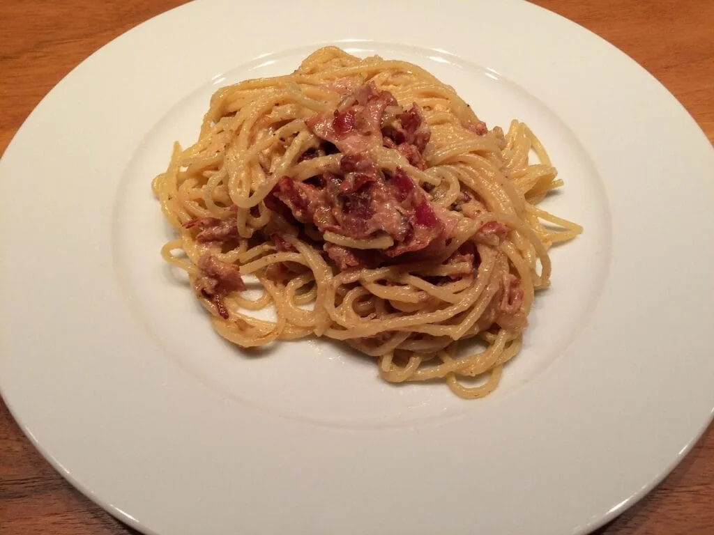 Portion de carbonara crémeuse sur assiette blanche, fond bois