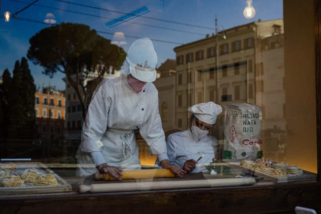 Deux cuisiniers façonnant des pâtes fraîches derrière une vitrine à Rome