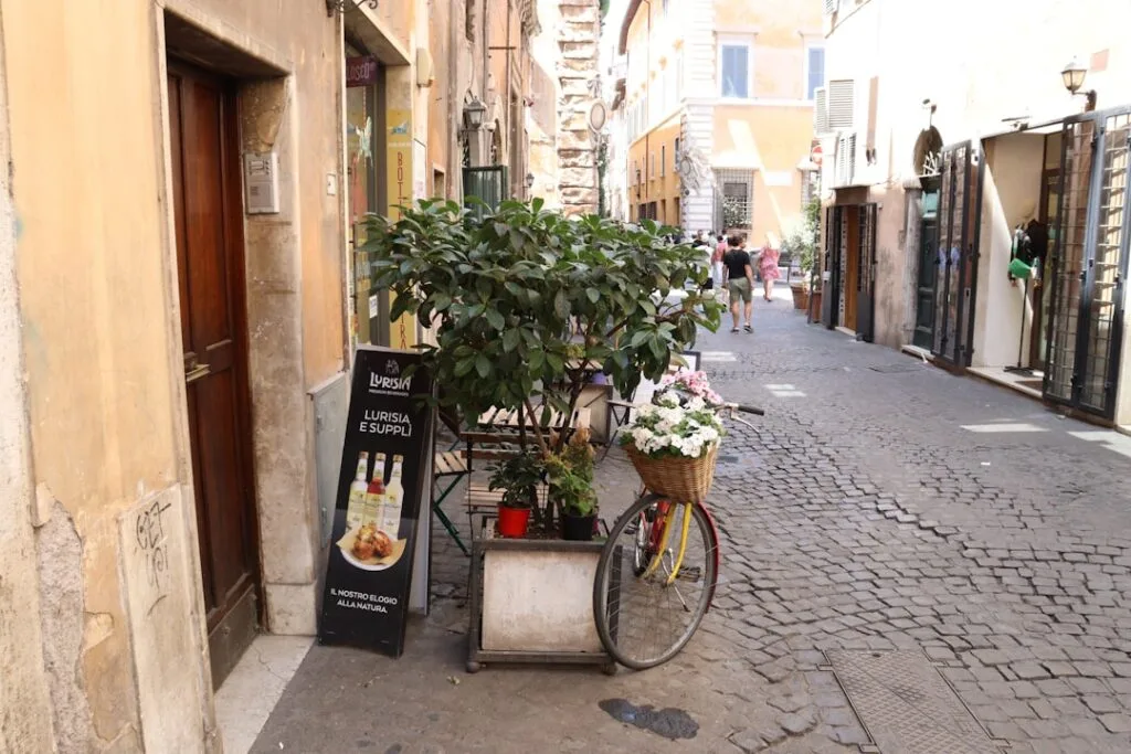 Rue pavée romaine avec vélo fleuri et panneau indiquant supplì